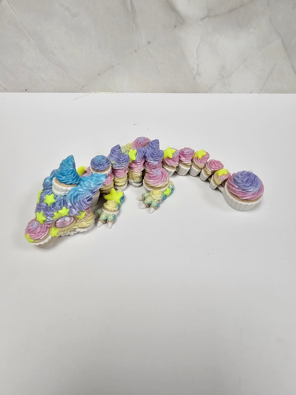 Made In Cobham articulated cupcake dragon figurine with pastel swirled frosting texture and bright yellow star accents.