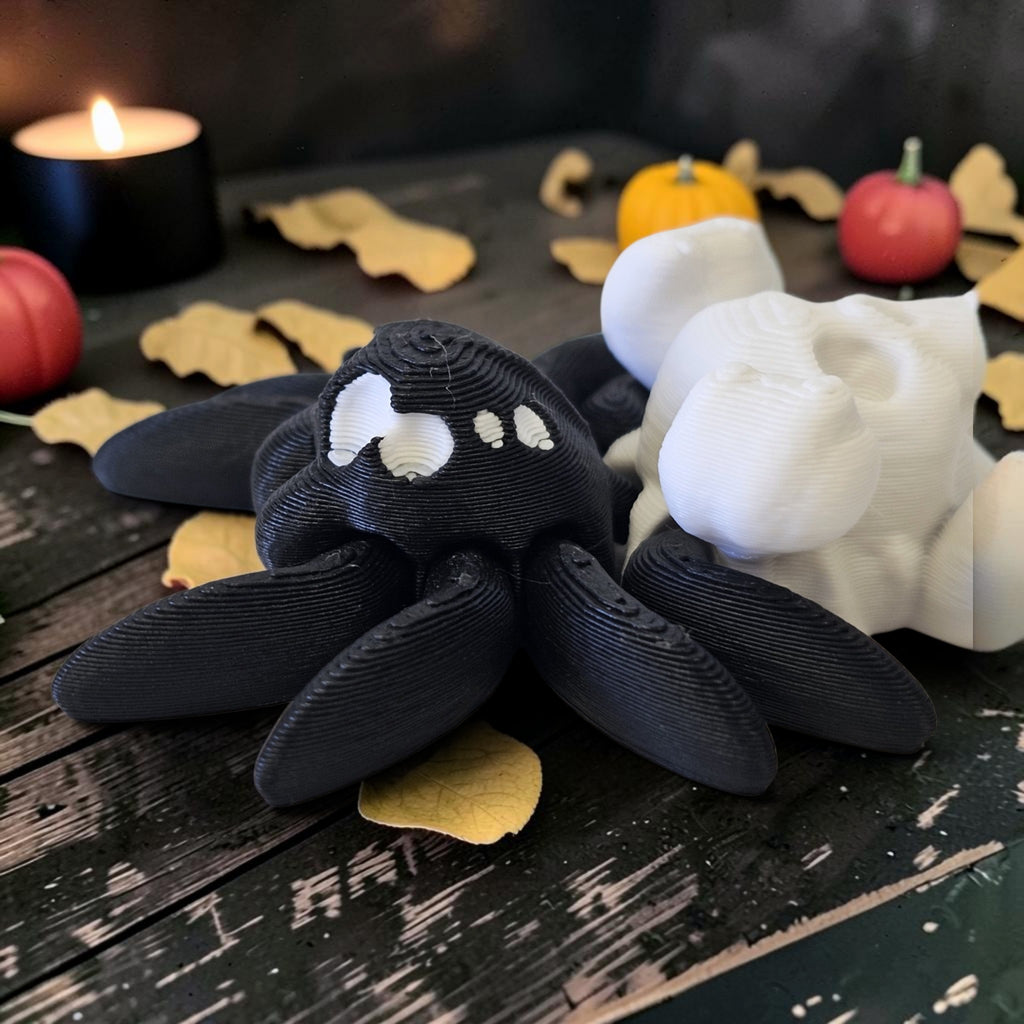 Made In Cobham articulated 3D-printed black and white spider figurines on a dark wooden table with Halloween decor.